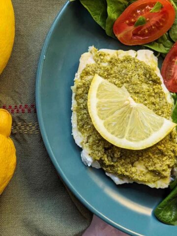A haddock fillet with a pesto topping on a plate with a fresh salad of spinach and tomatoes on the side.