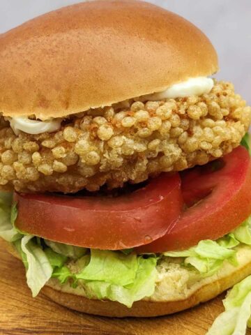 A chicken patty in a bun with salad and mayo, sitting on a kitchen board.