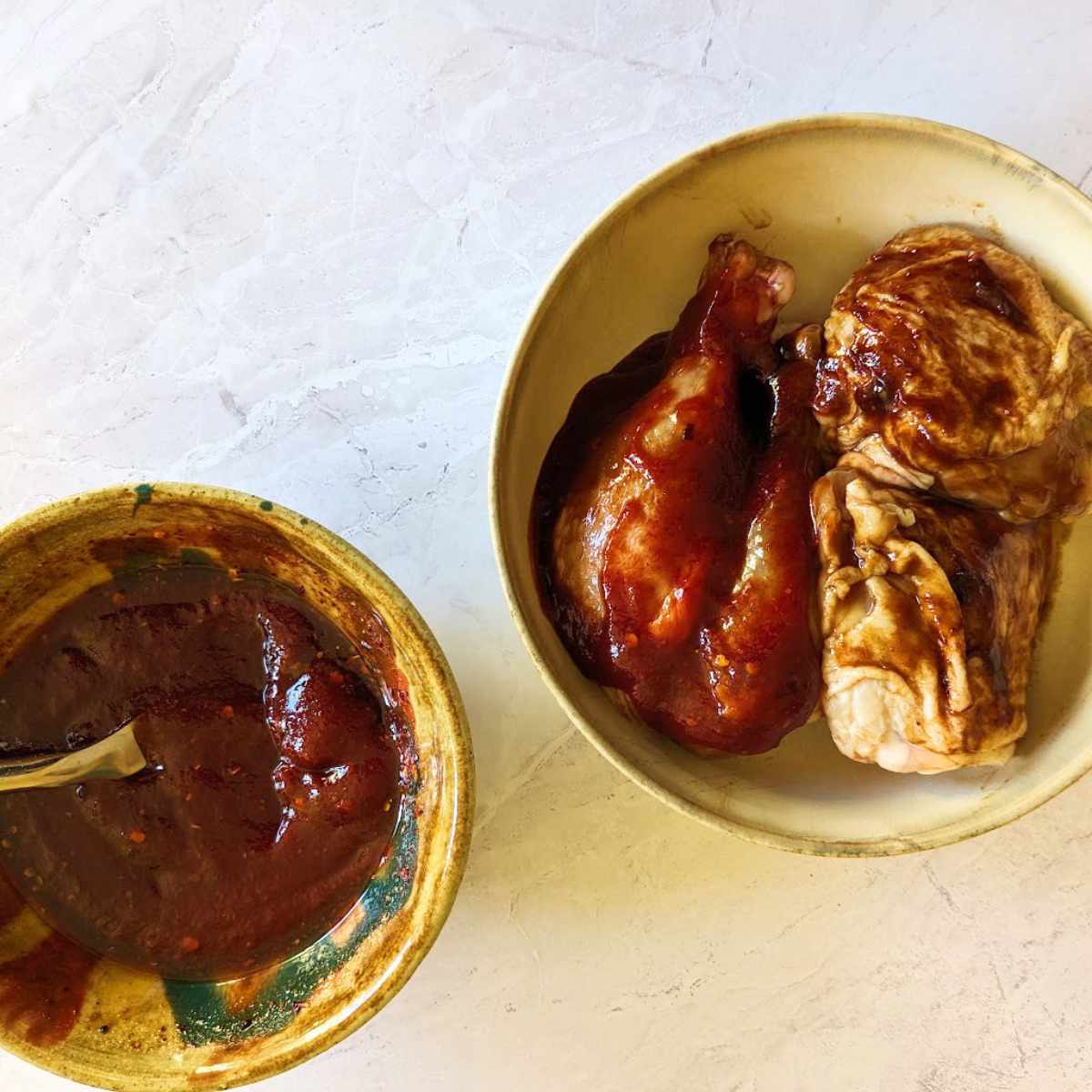 Chicken pieces in a bowl with a separate bowl of barbeque sauce alongside.