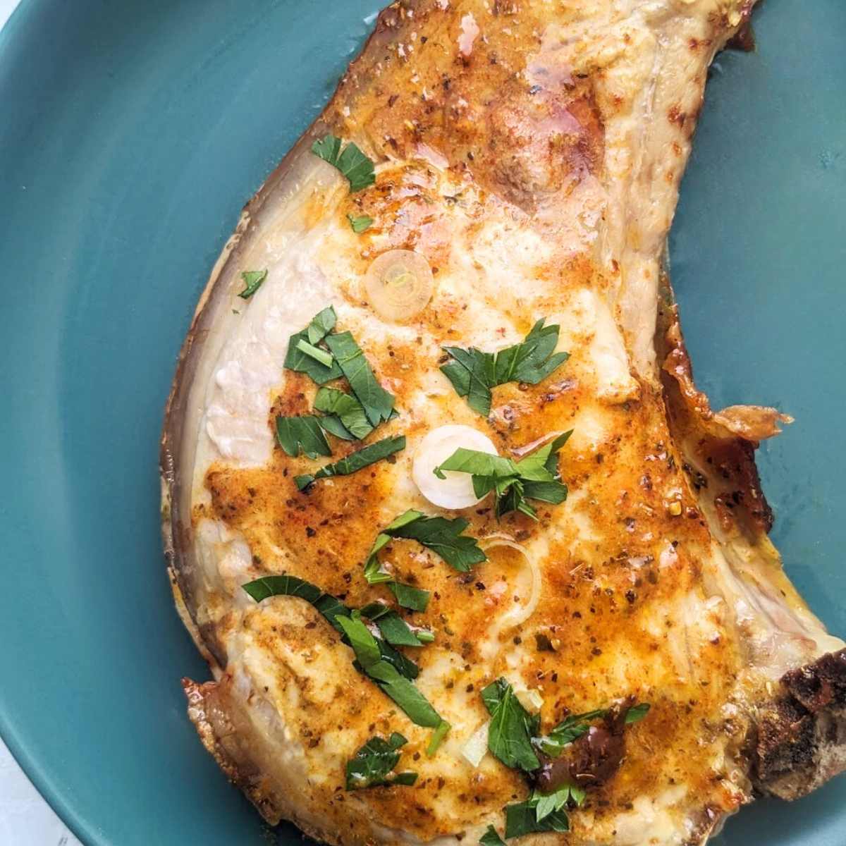 A pork chop with a glaze sits on top of a blue plate.