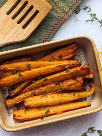 Air fryer roasted carrots in a serving dish with herbs scattered over.