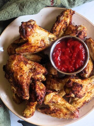 Air fryer chicken wings on a plate with a tomato dip.