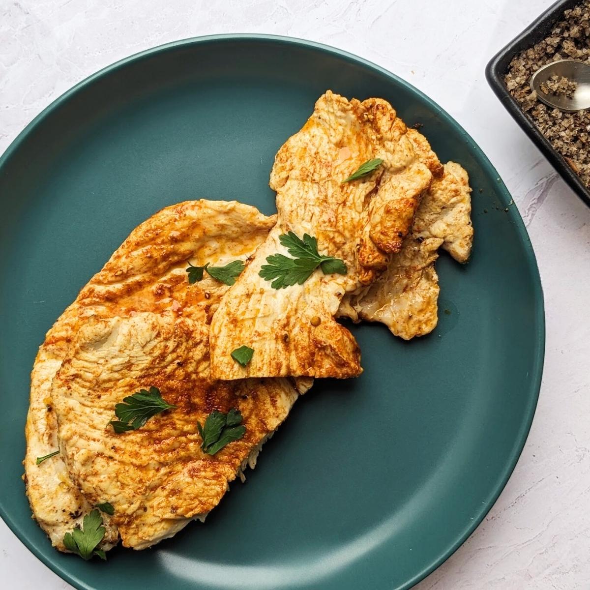 Two turkey breast steaks topped with herbs and spices on a blue plate.