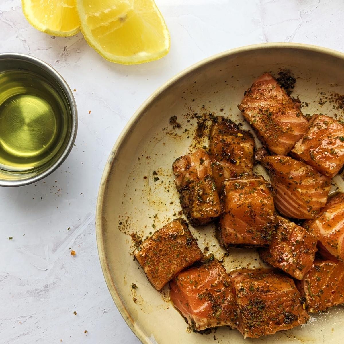 Salmon bites in a bowl with seasoning and lemon.