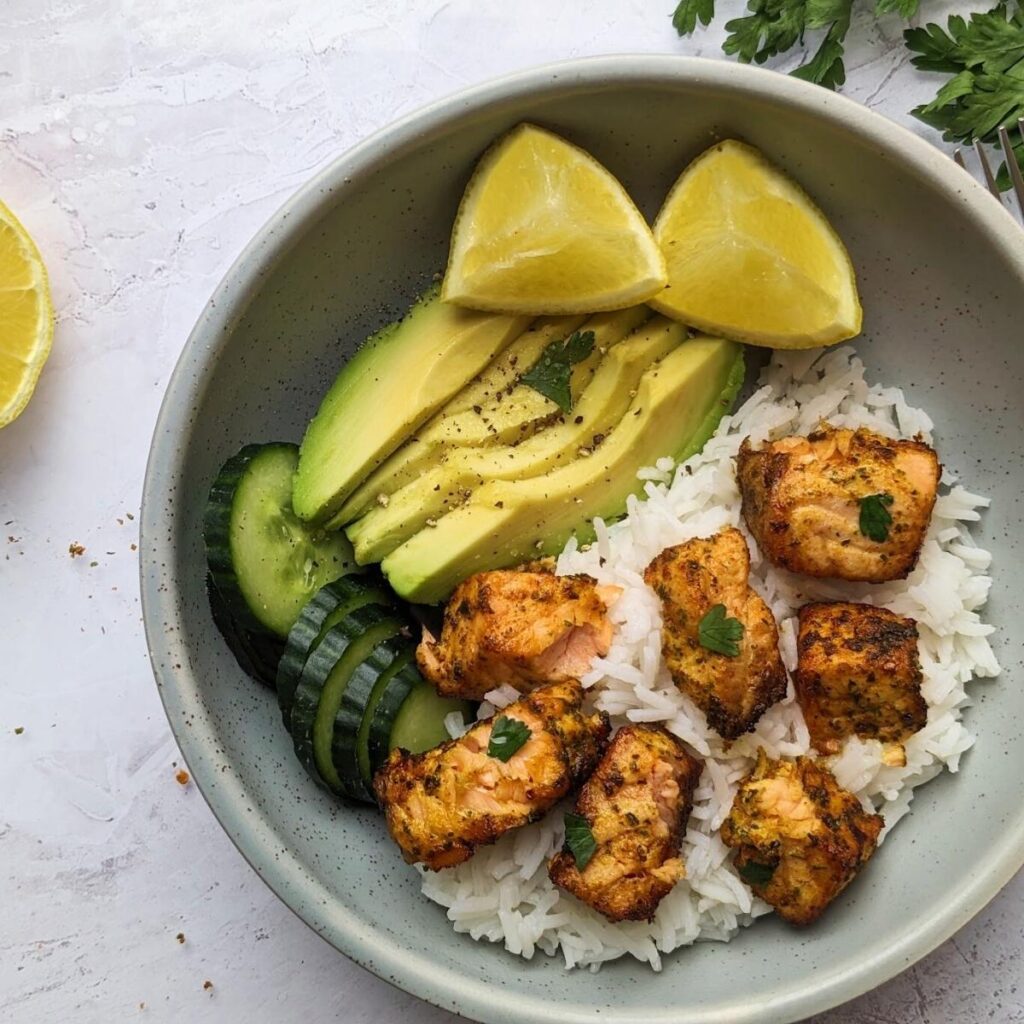 Salmon bites with rice, cucumber, avocado and lemon wedges.