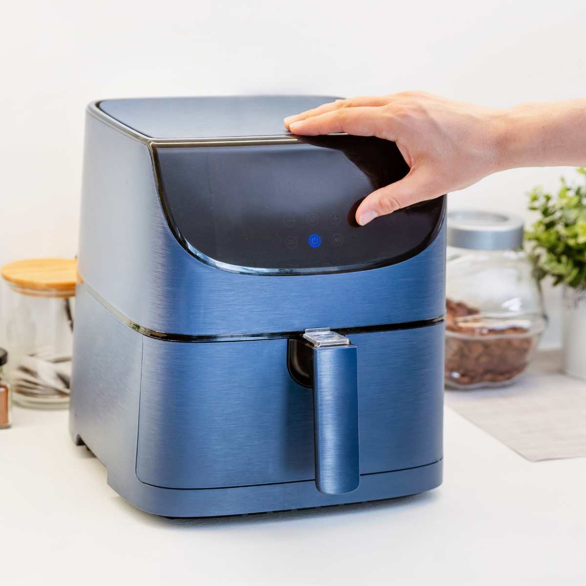 A small blue air fryer on a kitchen worktop with a hand resting on top.