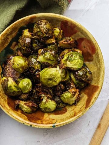 Balsamic Brussels sprouts in a bowl with a wooden spoon at the side.
