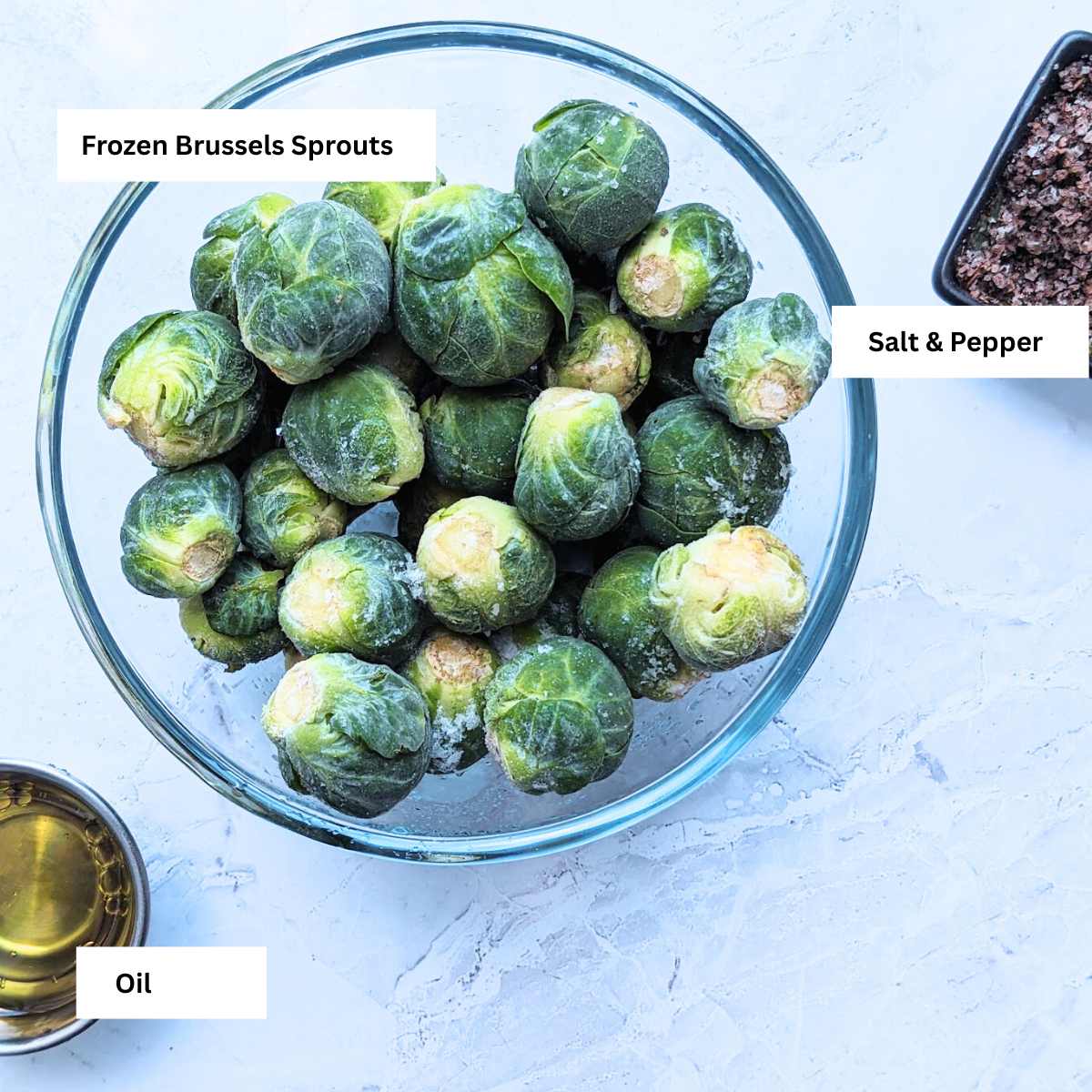 Ingredients for making frozen Brussels sprouts in an ainr fryer, including a bowl of frozen sprouts, salt and pepper and oil.