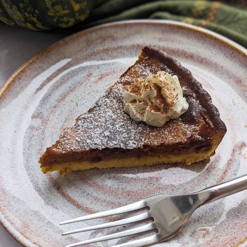 A slice of spicy pumpkin pie with cream, served on a round plate.
