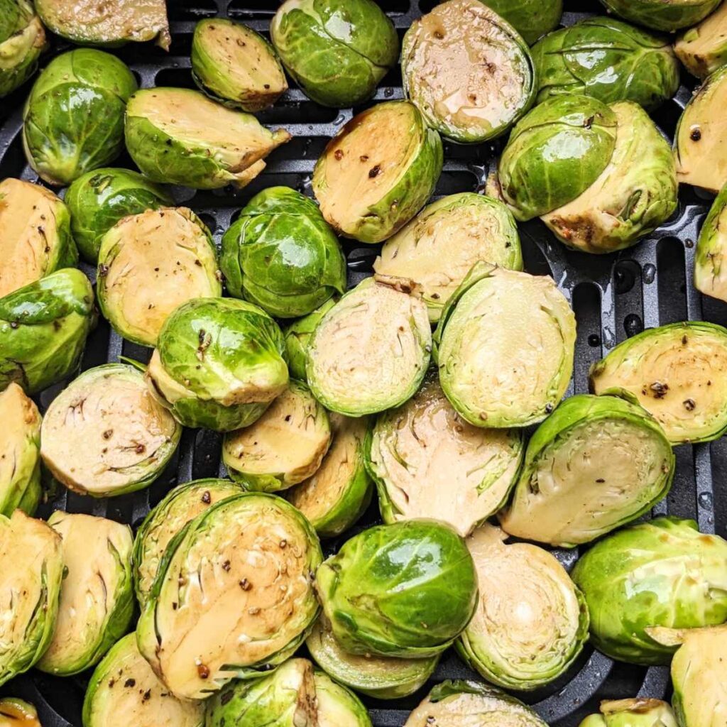 Halved Brussels Sprouts with seasoning in an air fryer basket.