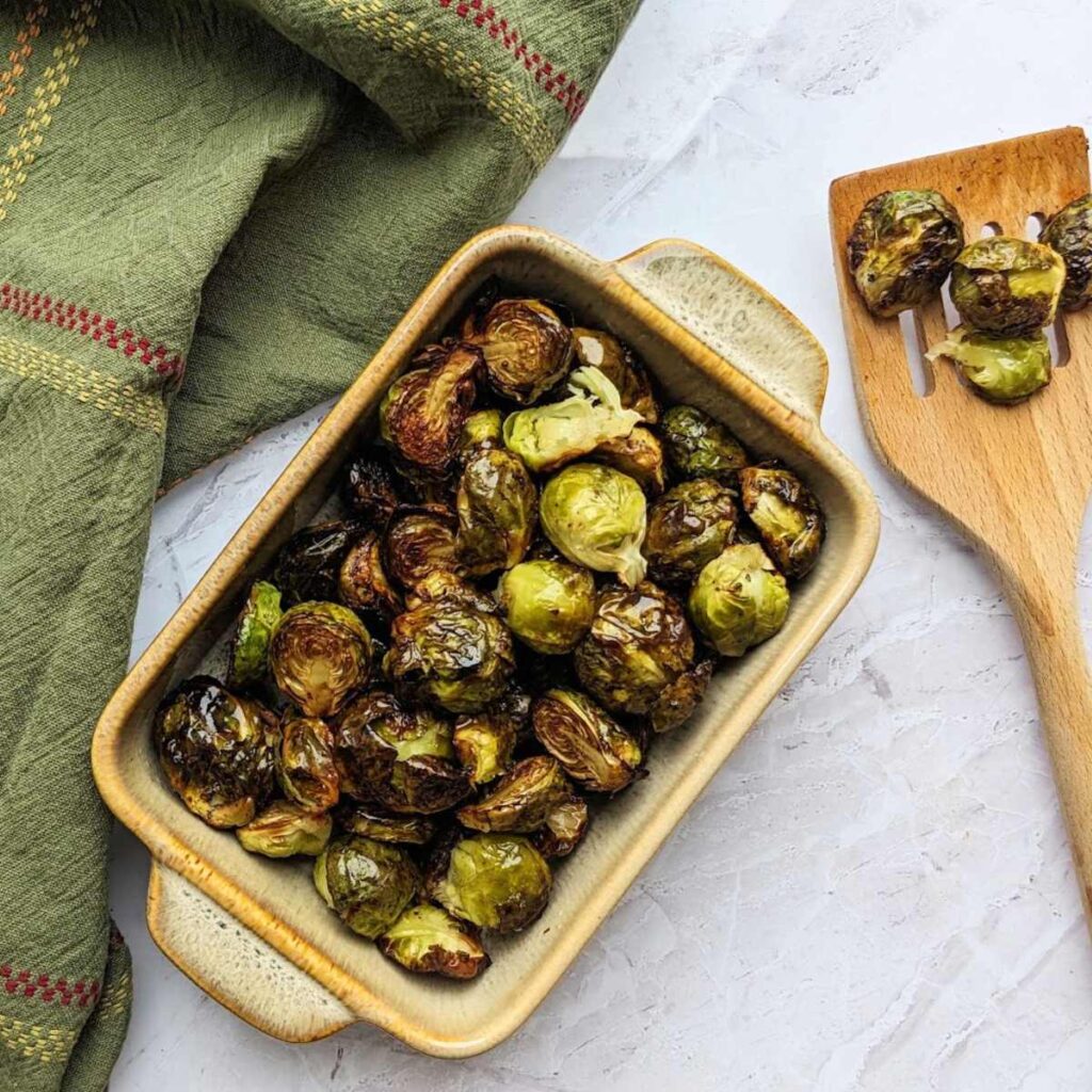 Air fried Brussels sprouts in a serving dish with a wooden serving spoon.