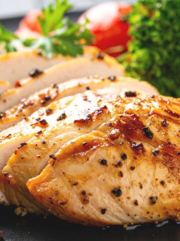 A sliced chicken breast with peppercorns on top on a plate with salad at the side.