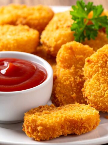 A white plate with a stack of air fried chicken nuggets alongside a small bowl of tomato ketchup dip.
