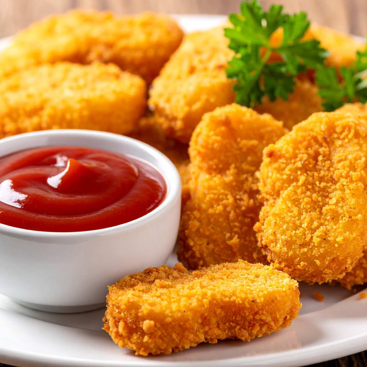 A white plate with a stack of air fried chicken nuggets alongside a small bowl of tomato ketchup dip.