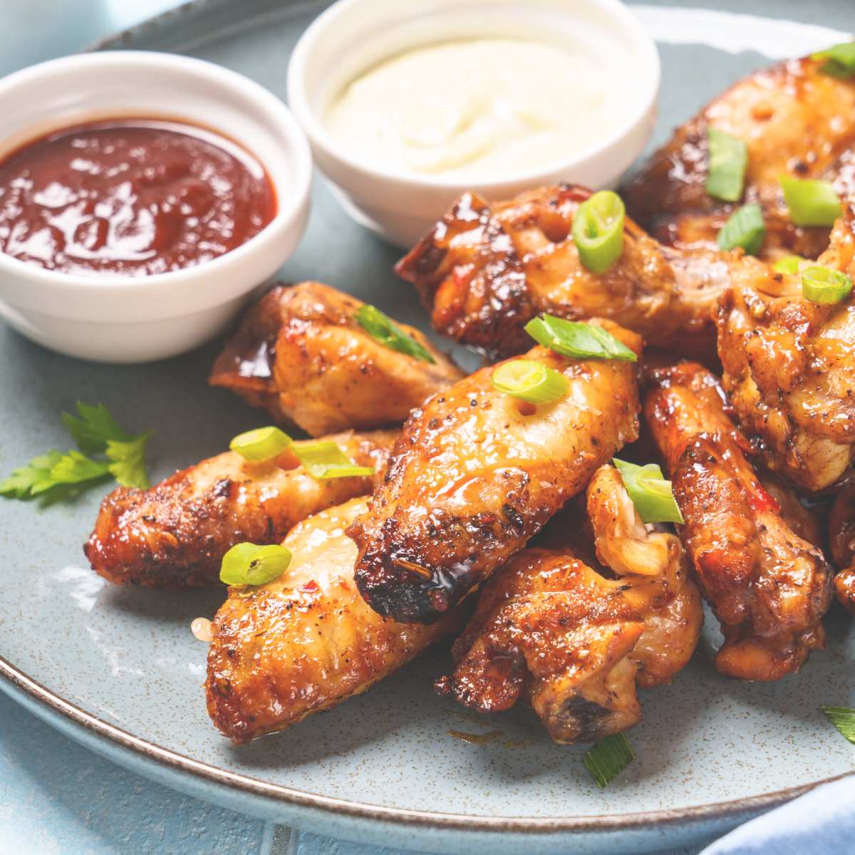  of chicken wings topped with slices of spring onion on a plate with dips at the side.