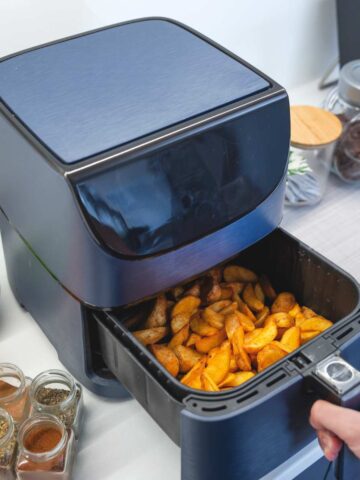 An air fryer basket opened to show the frozen chips inside.