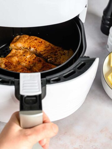 Salmon fillets in an air fryer drawer with a bowl of cut lemons at the side.