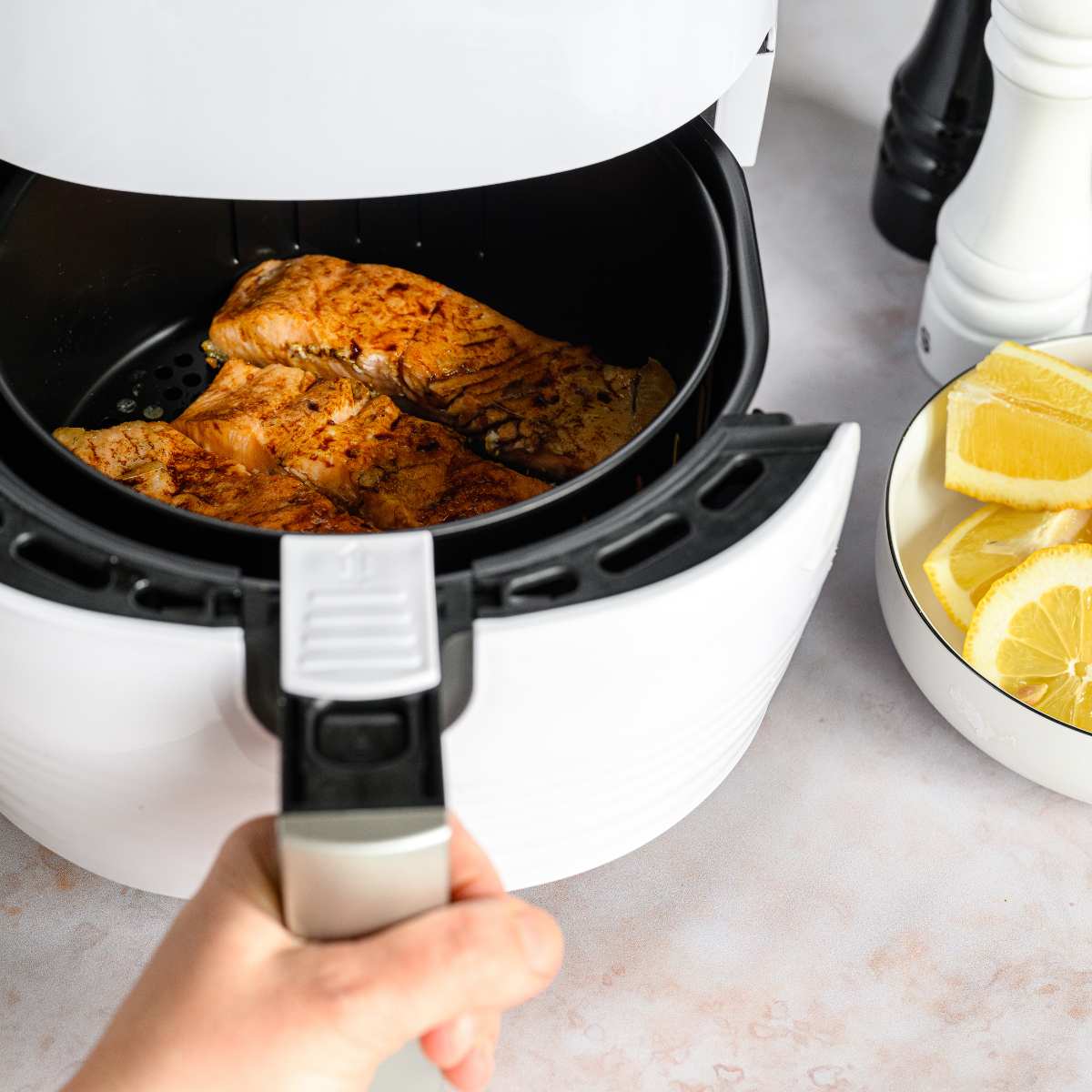 Salmon fillets in an air fryer basket with a bowl of freshly cut lemons at the side.